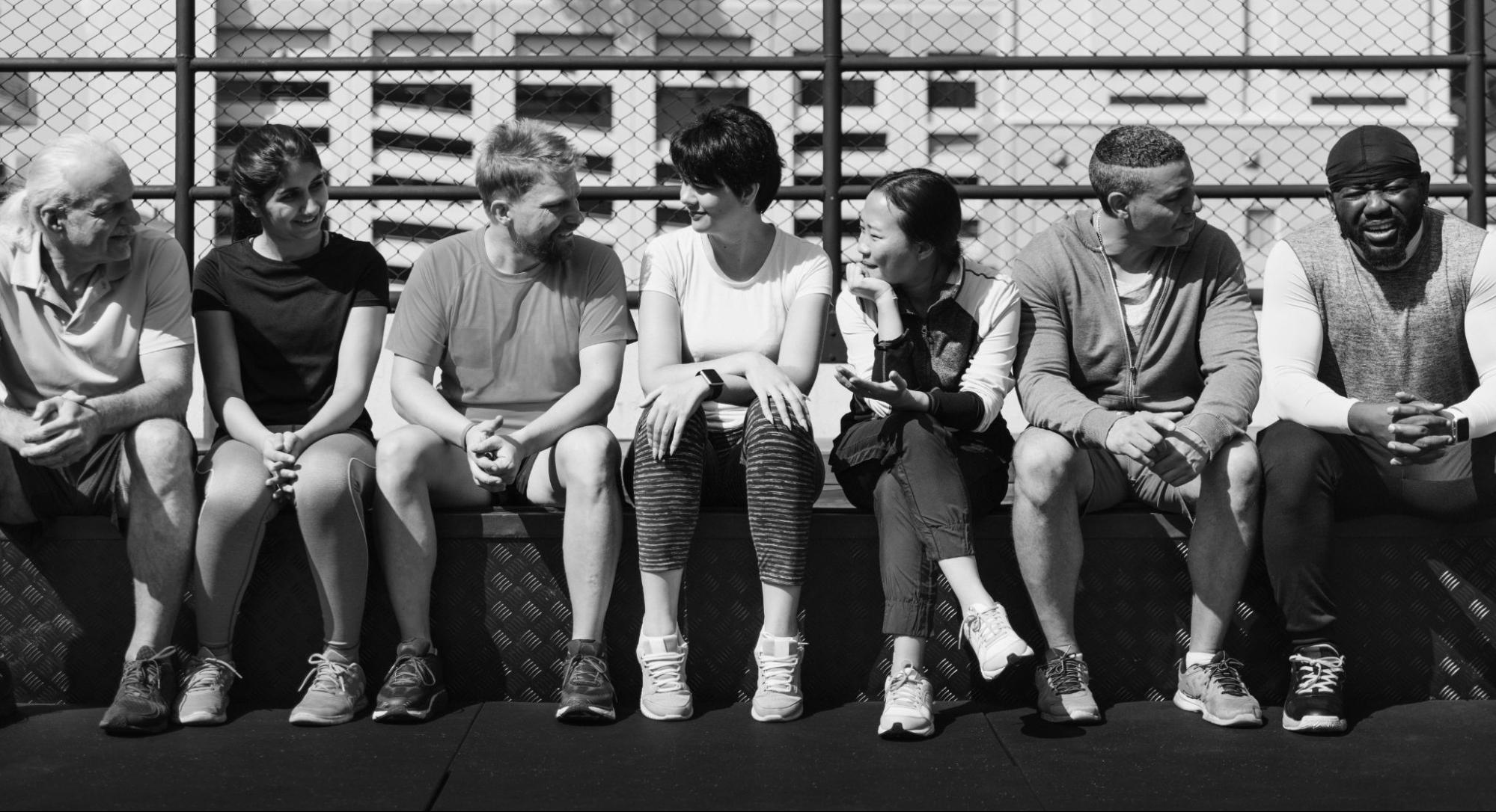 image1 Black-and-white photo of a diverse group of student-athletes sitting together on outdoor bleachers, smiling and talking.