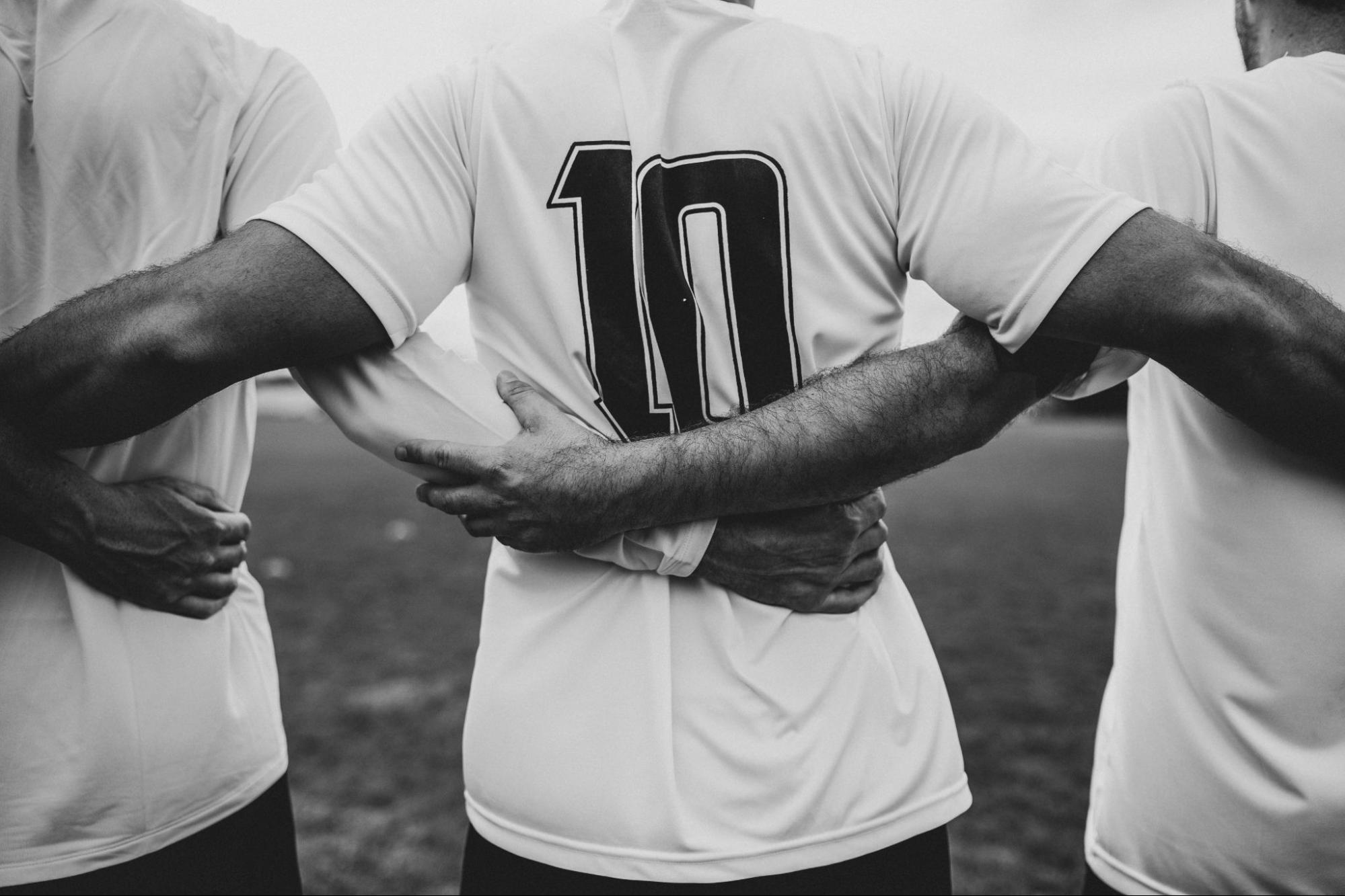 image2 Black and white picture of three football players in white jerseys linking arms on the field, representing team unity and discipline.